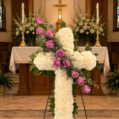 White floral cross with pink roses on an easel in a church