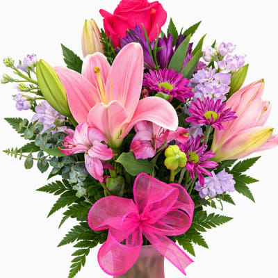 Pink lilies, roses, and purple flowers in a pink vase with a ribbon