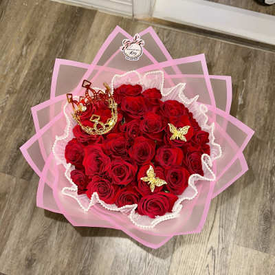 Bouquet of red roses wrapped in pink paper with gold crown accents