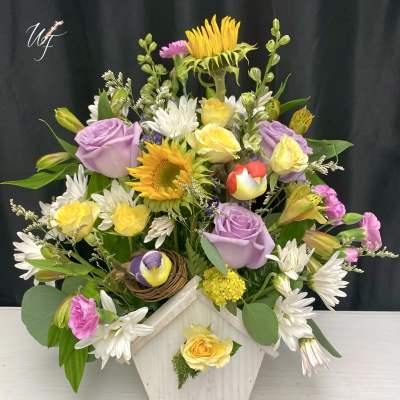 Mixed bouquet in a white wooden vase with sunflowers, roses, and daisies