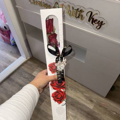 Two red roses in a tall white gift box with a black ribbon