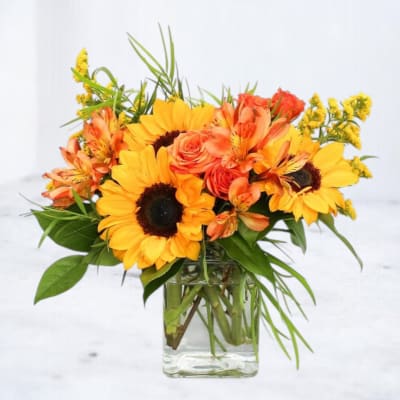 Sunflower and orange rose arrangement in a clear glass vase