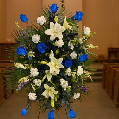 Standing floral spray with blue roses and white lilies on an easel
