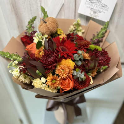 Bouquet of red, orange, and cream flowers wrapped in brown paper