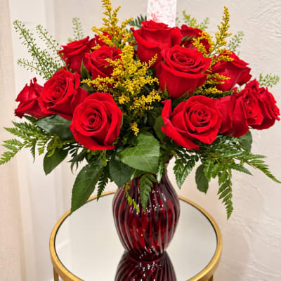 Red roses arranged in a burgundy glass vase with yellow filler flowers
