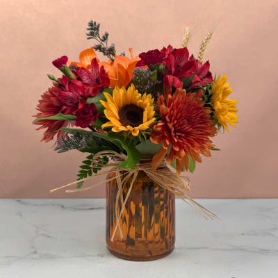 Mixed bouquet with sunflowers, orange and red blooms in an amber glass vase