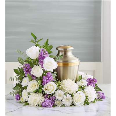 White roses and purple flowers arranged around a gold urn