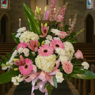 Pink and white floral arrangement with lilies, gerberas, and hydrangeas in a church