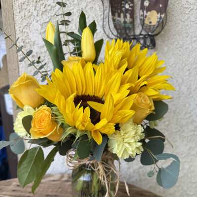 Yellow sunflower bouquet in a glass jar with roses and carnations