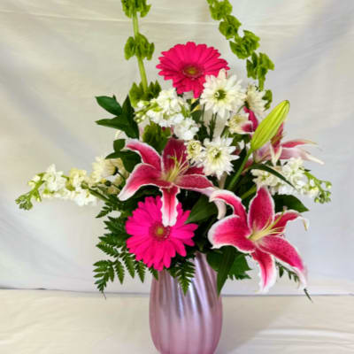 Tall pink and white arrangement with lilies and gerbera daisies in a pink vase with arching green bells of Ireland
