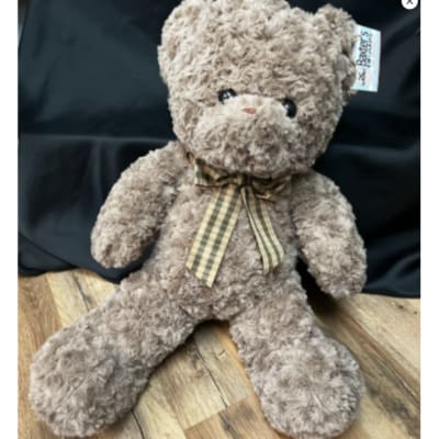 Plush teddy bear with a plaid ribbon bow sitting on a wooden floor