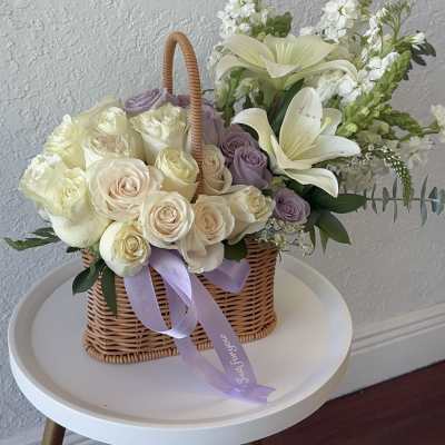 Basket of cream and lavender roses with white lilies and ribbon