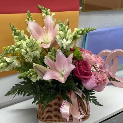 Pink lilies and roses arranged in a wicker basket with ribbon