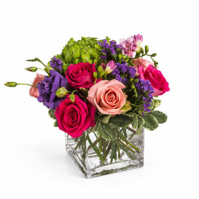Mixed pink, purple, and peach flowers in a clear square vase