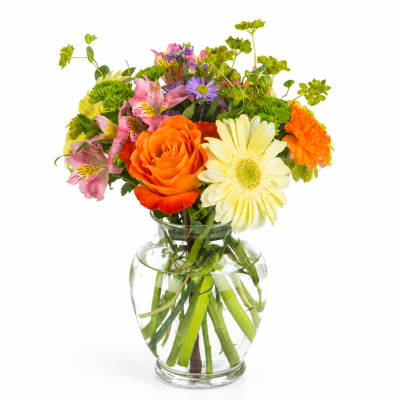 Mixed bouquet of orange, yellow, pink, and purple flowers in a clear glass vase