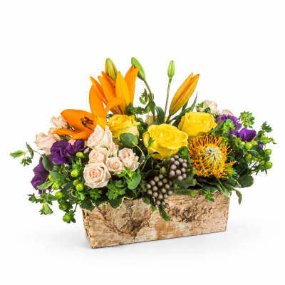 Mixed bouquet with orange lilies, yellow roses, and purple blooms in a rectangular basket