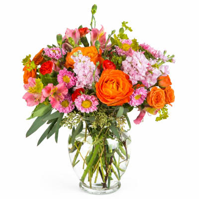 Mixed bouquet of orange, pink, and red flowers in a clear glass vase
