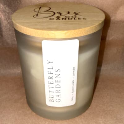 Frosted glass candle jar with a wooden lid labeled Butterfly Gardens