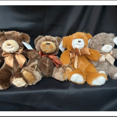 Four plush teddy bears with ribbon bows on a black fabric background
