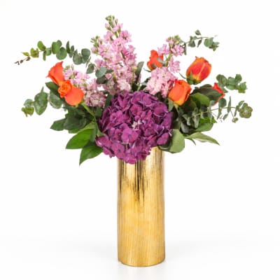 Purple hydrangea and orange roses in a tall gold vase