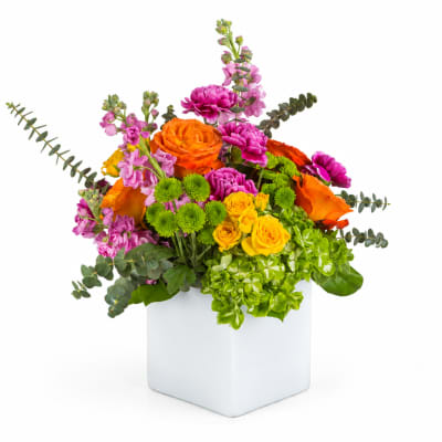 Colorful bouquet in a white square vase with orange, pink, yellow, and green blooms