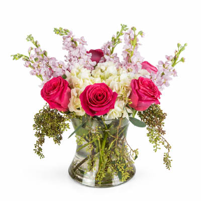 Pink roses and pale flowers arranged in a clear glass vase