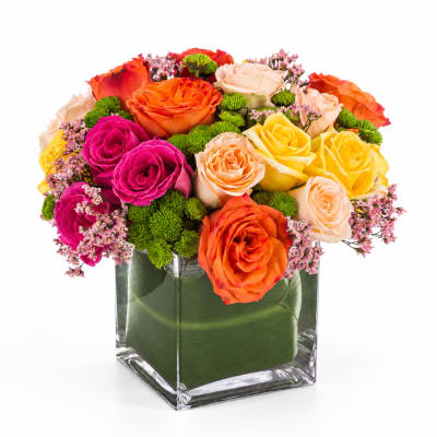 Colorful roses in a clear square vase with green accents