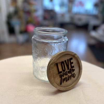 Clear glass jar with a wooden lid engraved "LOVE you more"