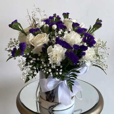 White and purple floral arrangement in a marble-patterned box with a ribbon