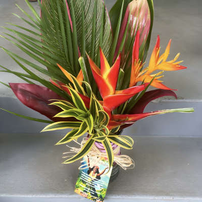 Tropical arrangement with orange-red heliconia and variegated foliage in a wrapped vase