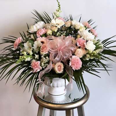 Pink and white floral arrangement in a white vase with a pink ribbon