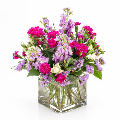 Pink and lavender flowers arranged in a clear square glass vase