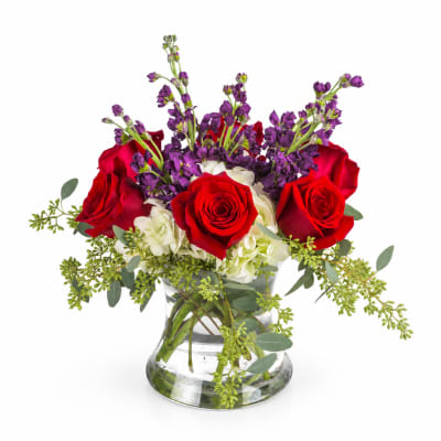 Red roses and purple flowers arranged in a clear glass vase