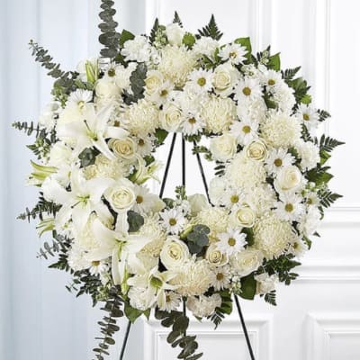 White floral wreath on a black stand with roses, daisies, and lilies