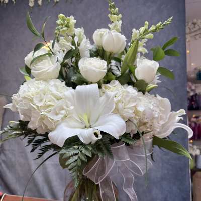 White lilies, roses, and hydrangeas in a glass vase with a sheer ribbon