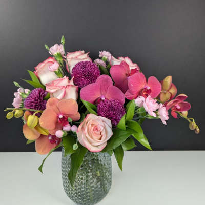 Pink and purple arrangement of roses, orchids, and mums in a textured glass vase