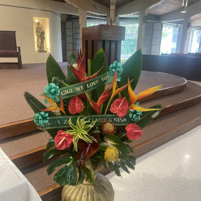 Tropical floral arrangement with red and orange blooms in a gold vase
