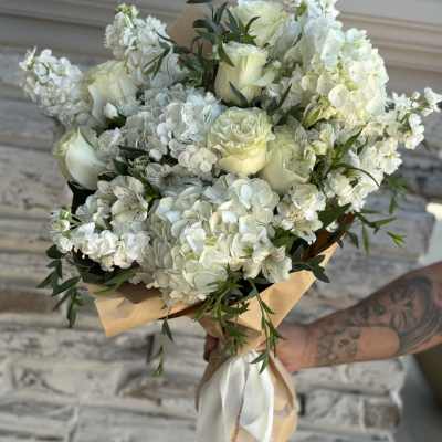 White rose and hydrangea bouquet wrapped in tan paper with a white ribbon