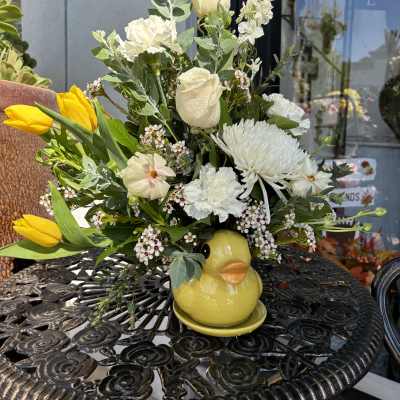 Bouquet of white flowers and yellow tulips in a yellow duck vase
