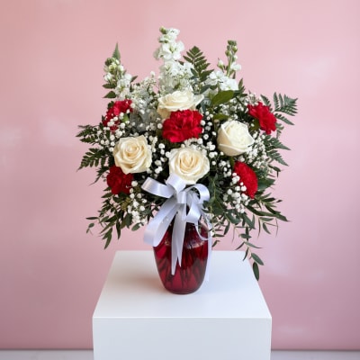 Red and white roses arranged in a red vase with a white ribbon