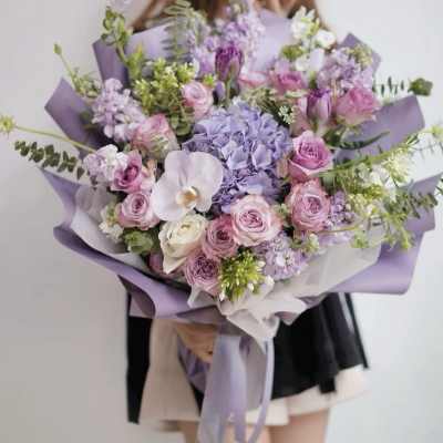 Large bouquet of pink and lavender flowers wrapped in purple paper