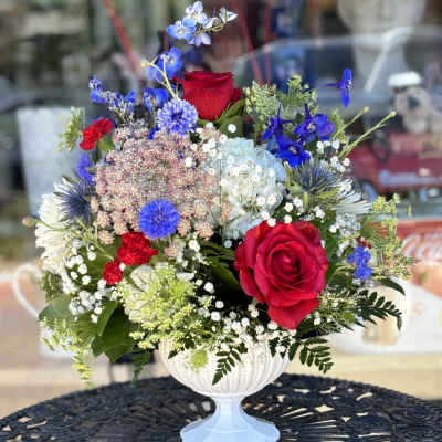 Mixed bouquet of red roses and blue flowers in a white pedestal vase