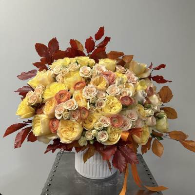 Large bouquet of yellow and peach roses in a white vase with autumn leaves