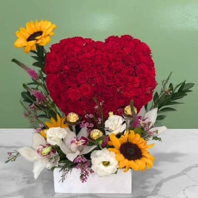 Heart-shaped red rose arrangement with sunflowers and white flowers in a white box