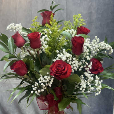 Red roses and white baby's breath in a clear glass vase with a red ribbon