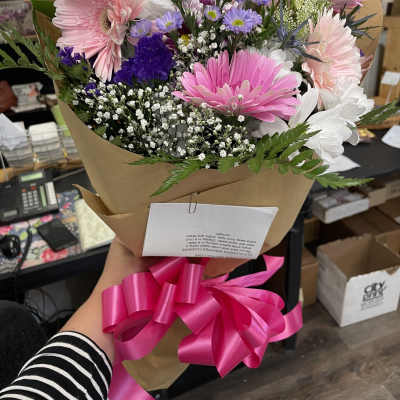 Bouquet of pink, white, and purple daisies wrapped in brown paper with a pink ribbon