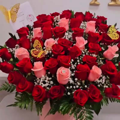 Pink and red roses arranged in a pink hatbox with butterfly picks