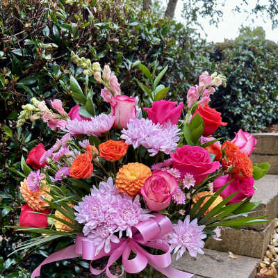 Pink and orange mixed flower bouquet in a glass vase with a pink ribbon