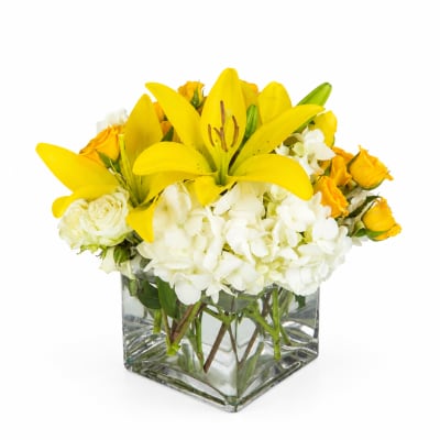 Yellow lilies and white flowers in a square glass vase