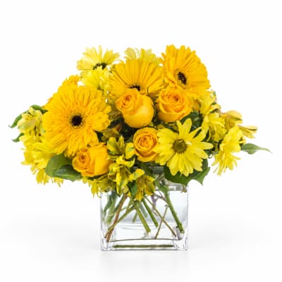 Yellow flowers and roses arranged in a clear glass vase